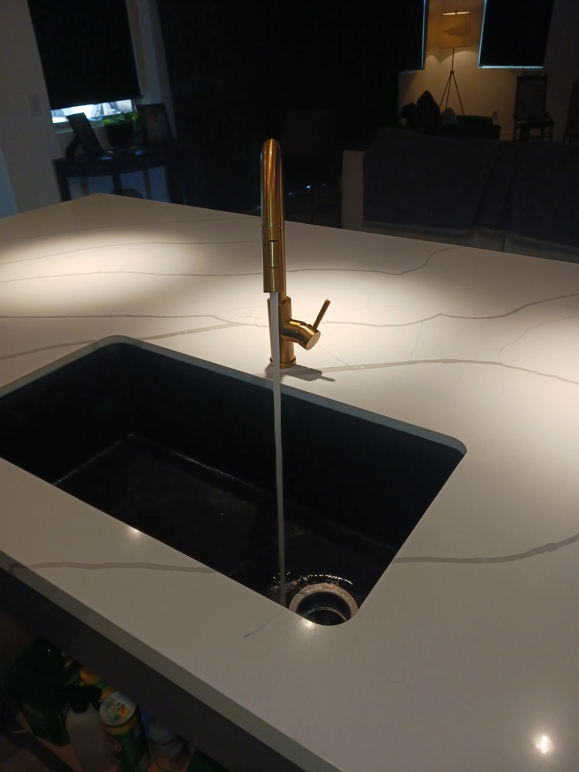 Black undermount kitchen sink with a polished brass single-handle pull-down faucet on a quartz island