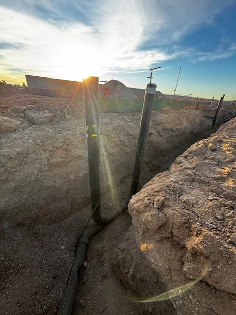 Vertical drain-line stub-outs set in trench at a new-construction site at sunset