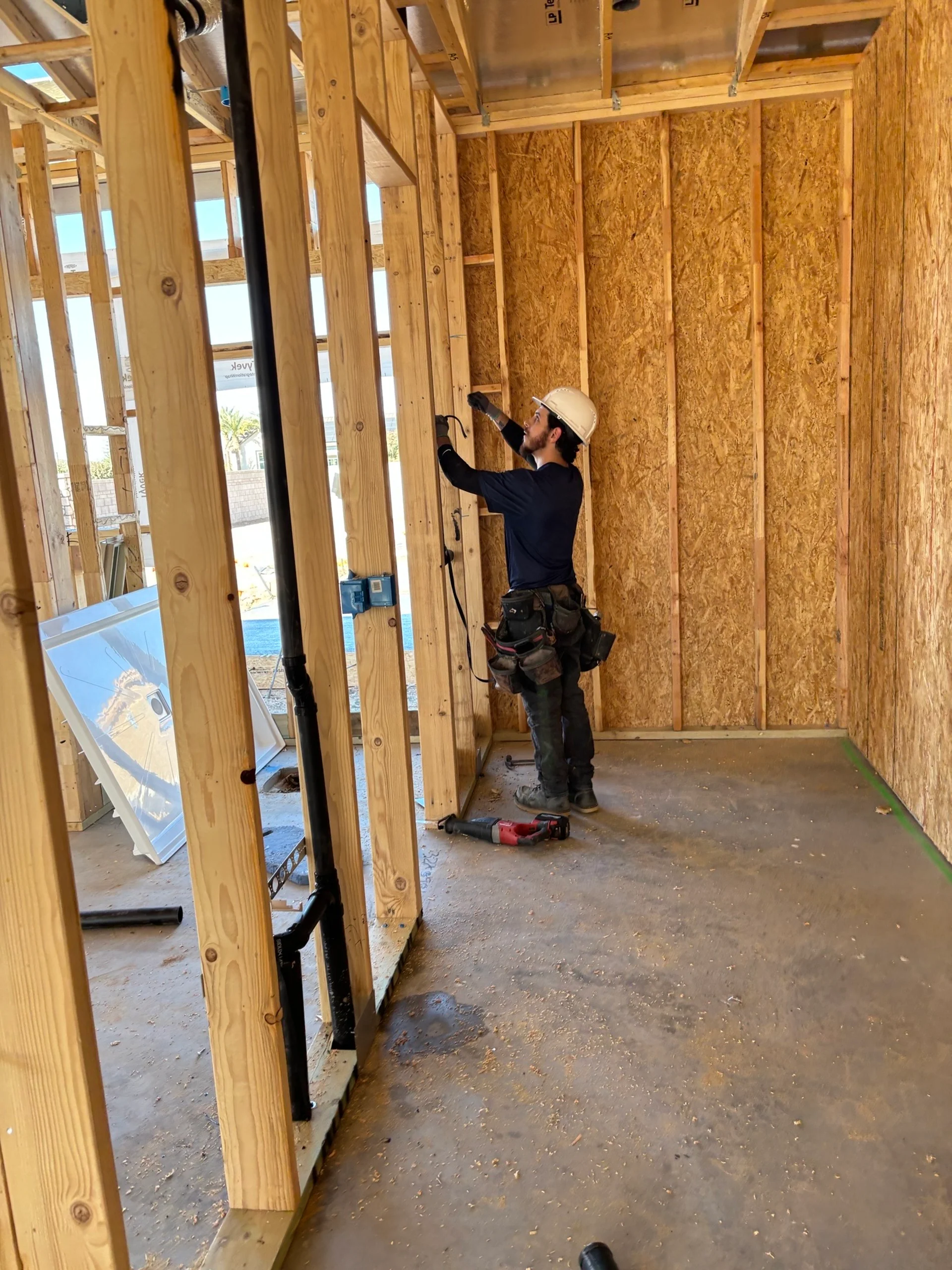 Ancla plumber in a hard hat marking out a wall during the framing/rough-in stage of a new construction job