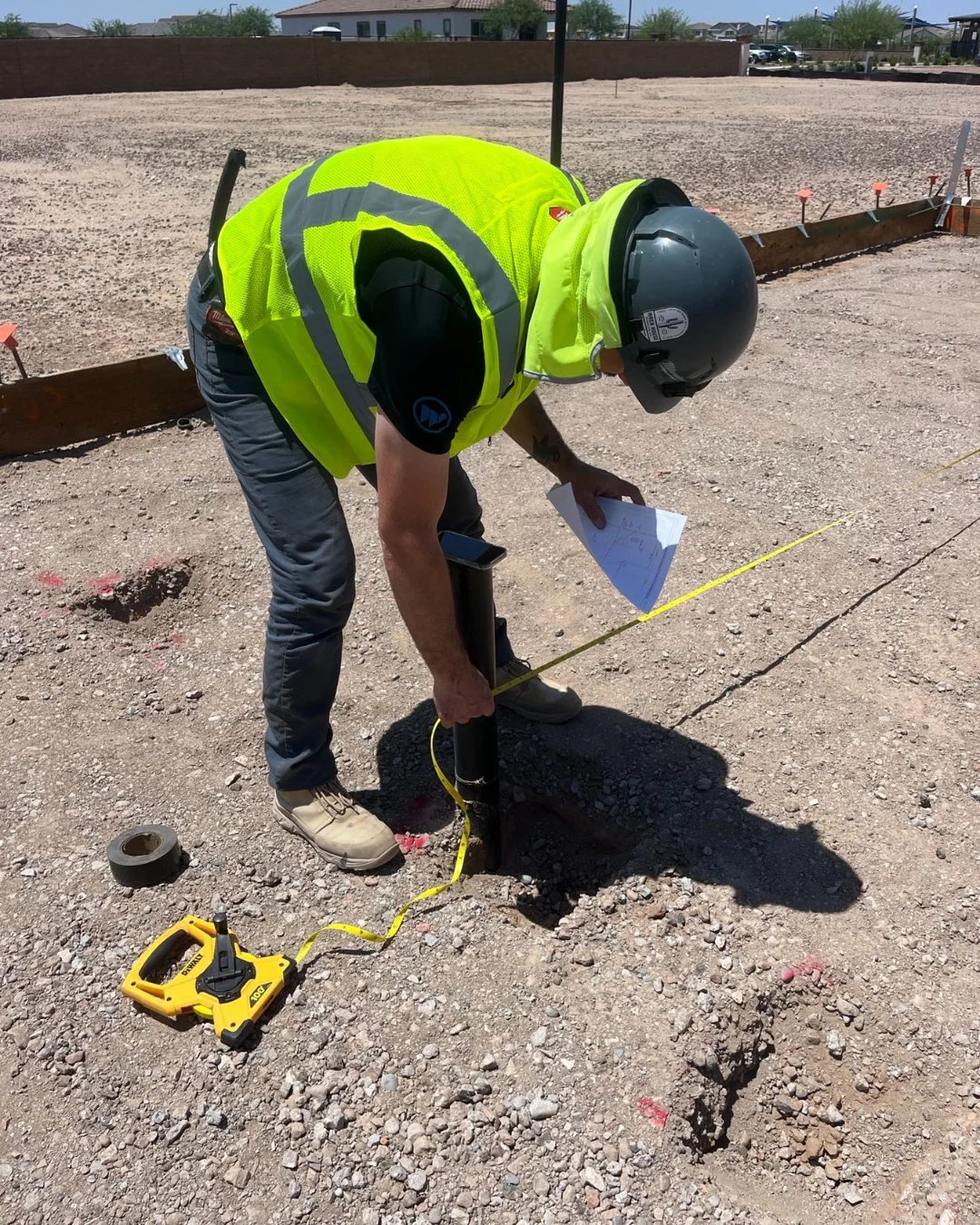 Crew member measuring and marking a water-service stub-out at a job site in safety yellow and a hard hat