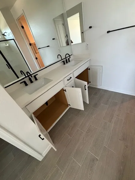 Bathroom double vanity with white quartz top, matte-black faucets, undermount sinks, and open shaker drawers below