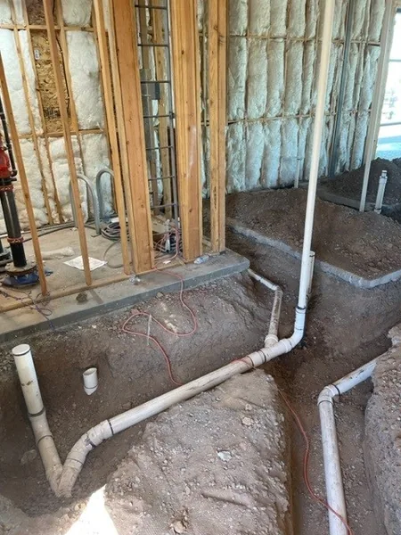 PVC drain stub-outs running through framed wall openings during rough-in, with spray-foam insulation between studs
