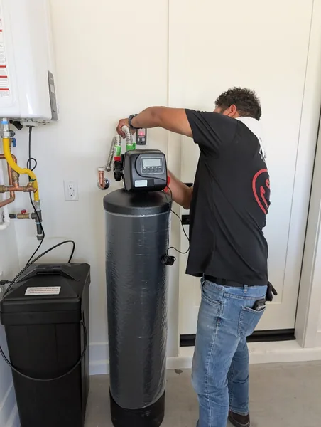 Ancla plumber installing a whole-home water softener in a residential garage