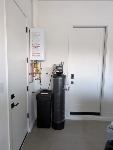 Tankless water heater mounted high on a garage wall with a whole-home water softener and brine tank below
