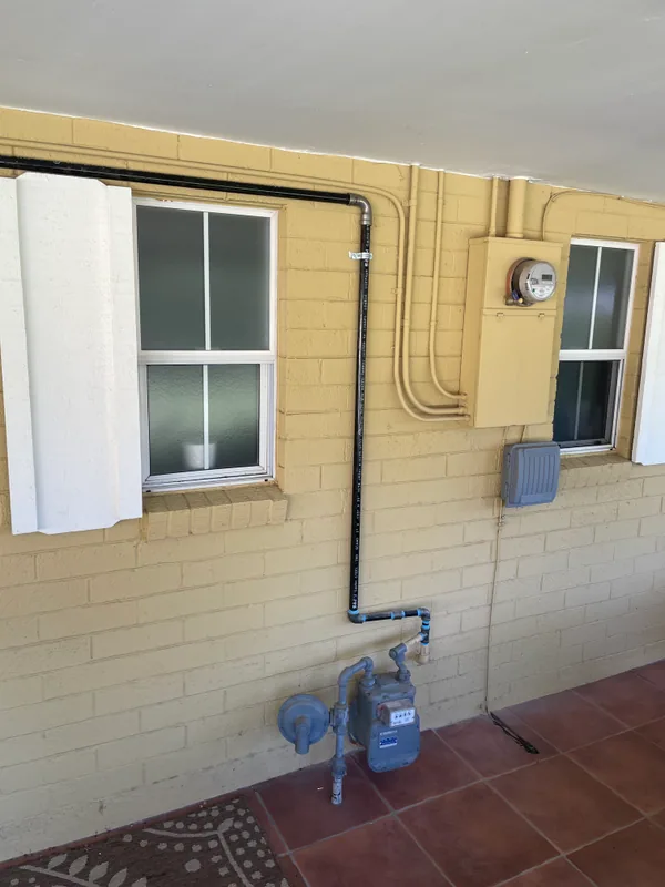 Black-iron gas line and meter feeding a tankless heater on an exterior stucco wall