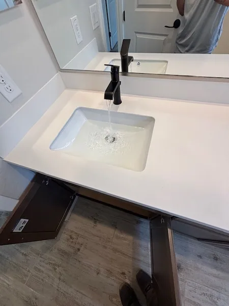 Matte-black single-handle faucet running water into a white quartz undermount bathroom vanity sink